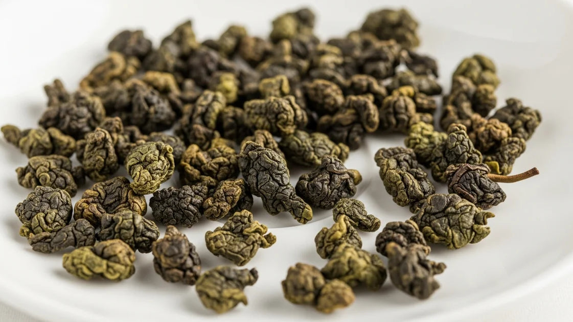 Rolled oolong tea leaves in a porcelain bowl showing amber and green tones