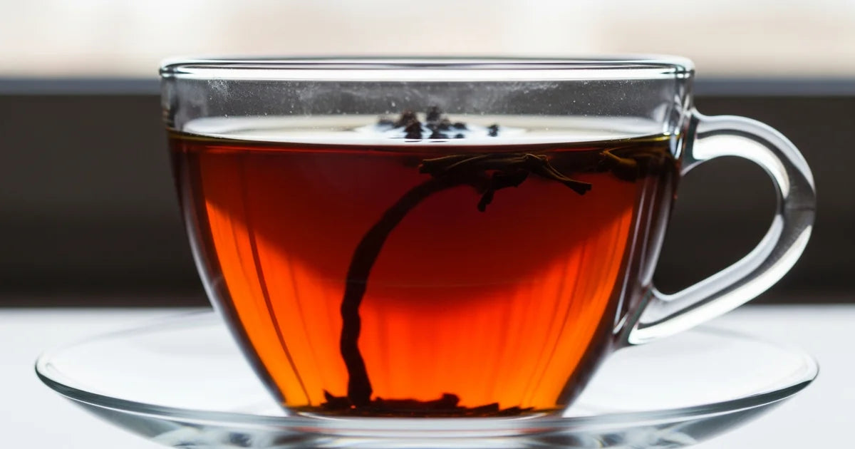 Black tea leaves in a rustic ceramic cup showing deep copper-red brew